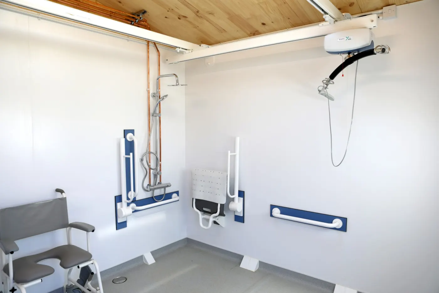 The ceiling track hoist above the level-access shower, with a fold-down seat and grab rails