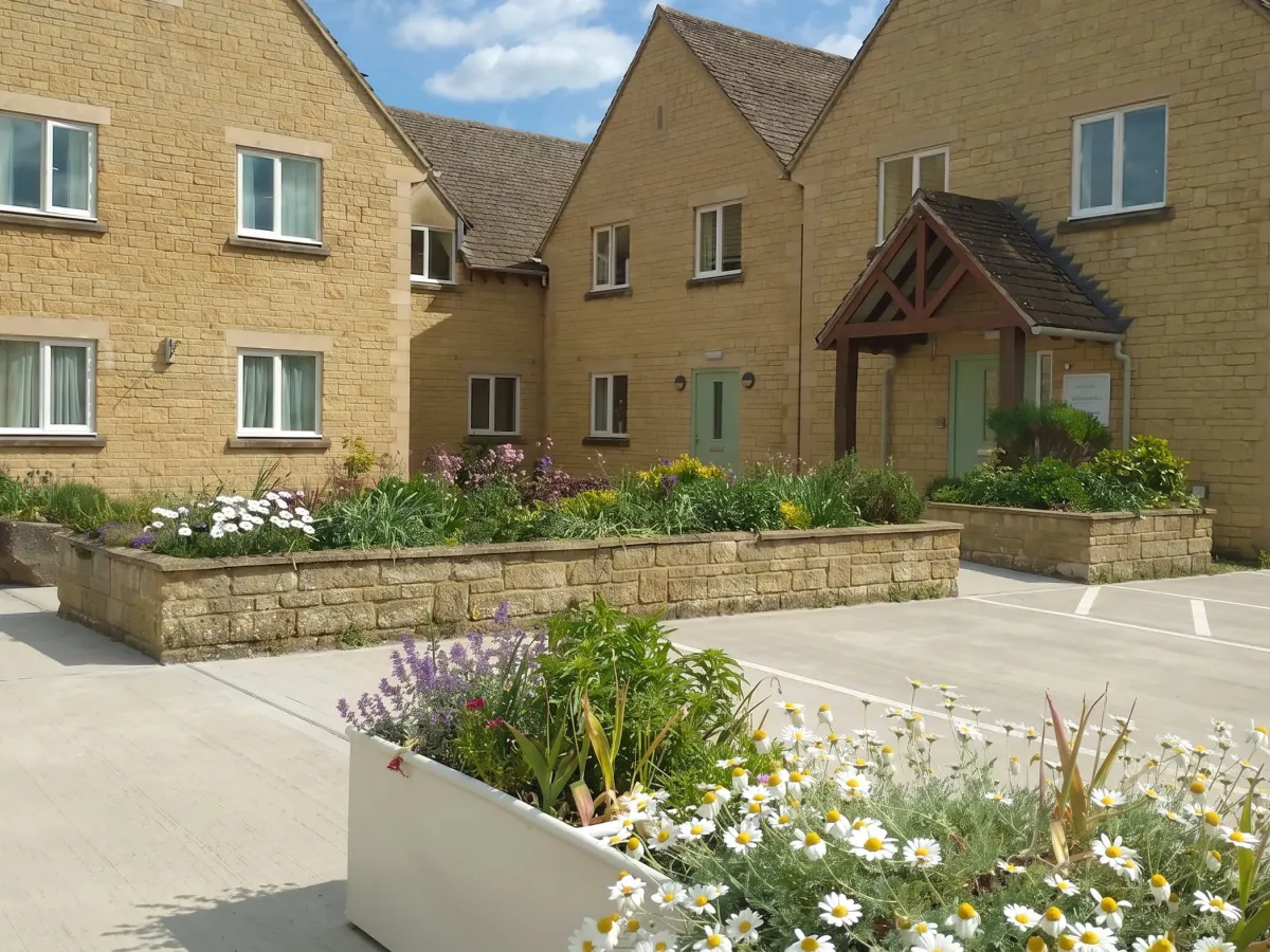 Wellspring in summer: Cotswold stone, sage green doors and flower beds full of daisies