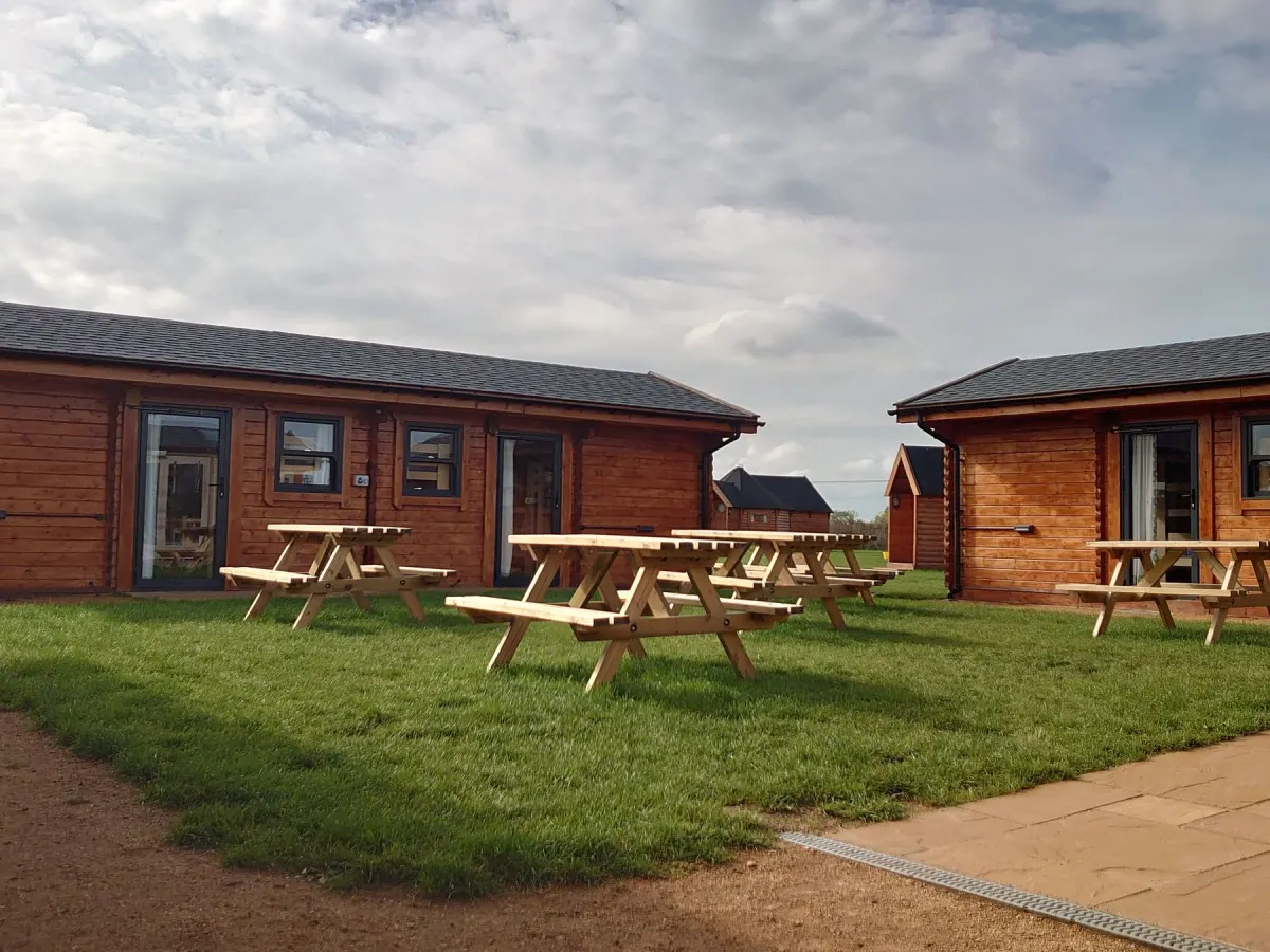 Timber cabins with picnic tables on the grass outside